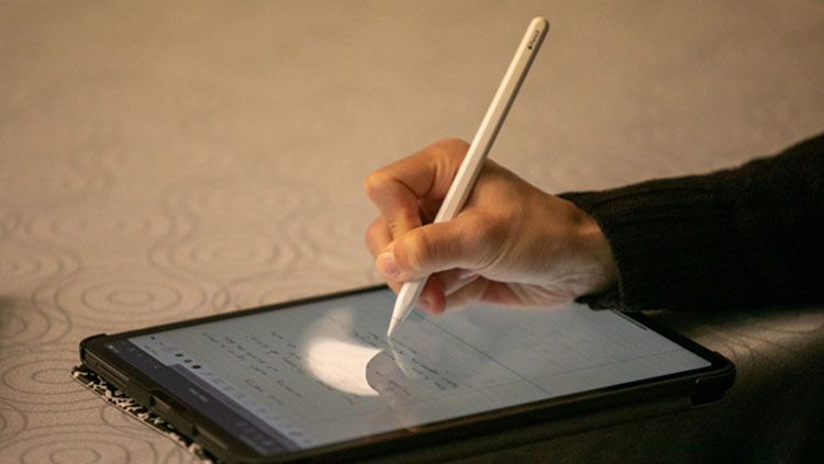 Image of someone's hand writing with a stylus on a tablet.