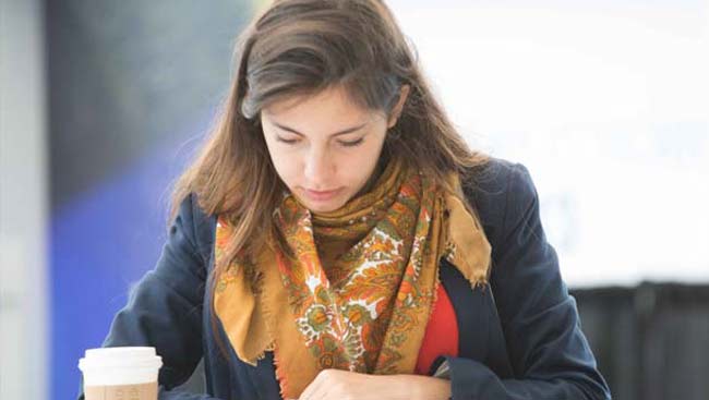 A female student reviews her notes wearing a scarf and holding a coffee cup.