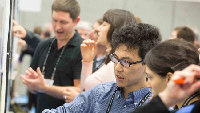 Male and female neuroscientists discuss scientific posters at SfN’s annual meeting.