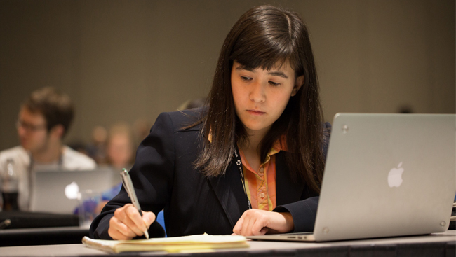 Young Woman in Business Attire with Laptop Open Taking Notes During Lecture