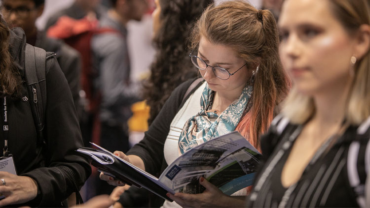 A woman intently reads a book in a crowd.