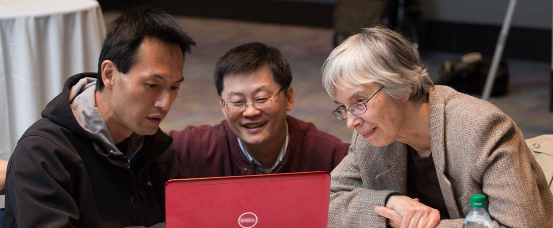 Three people sit around a red laptop having a discussion