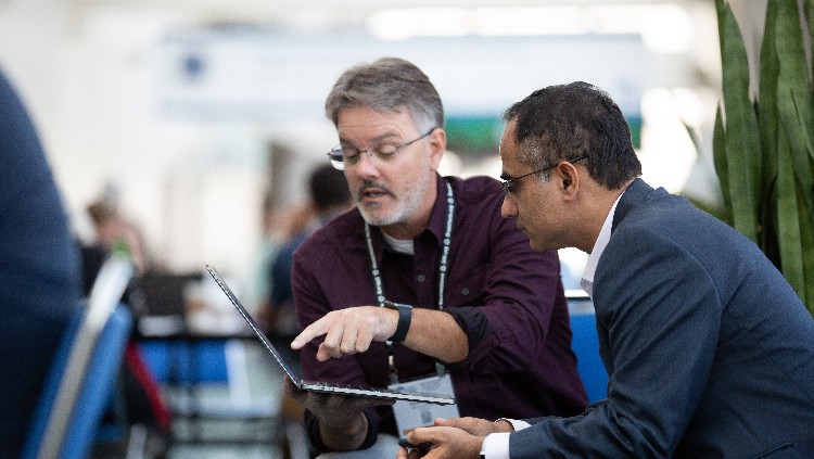 Annual meeting attendees talking to each other while holding a laptop