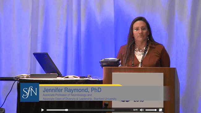 Jennifer Raymond stands at a podium and talks to neuroscientists about how challenges in the field can bring change. 