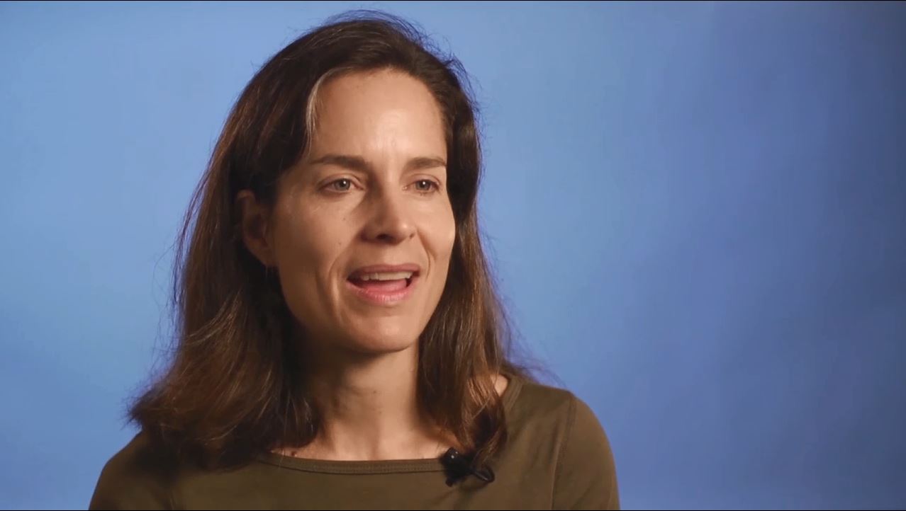 Female neuroscientist sits in front of a blue background talks about success in academia.