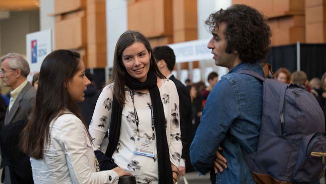 Two females and a male engage in conversation at a conference. 