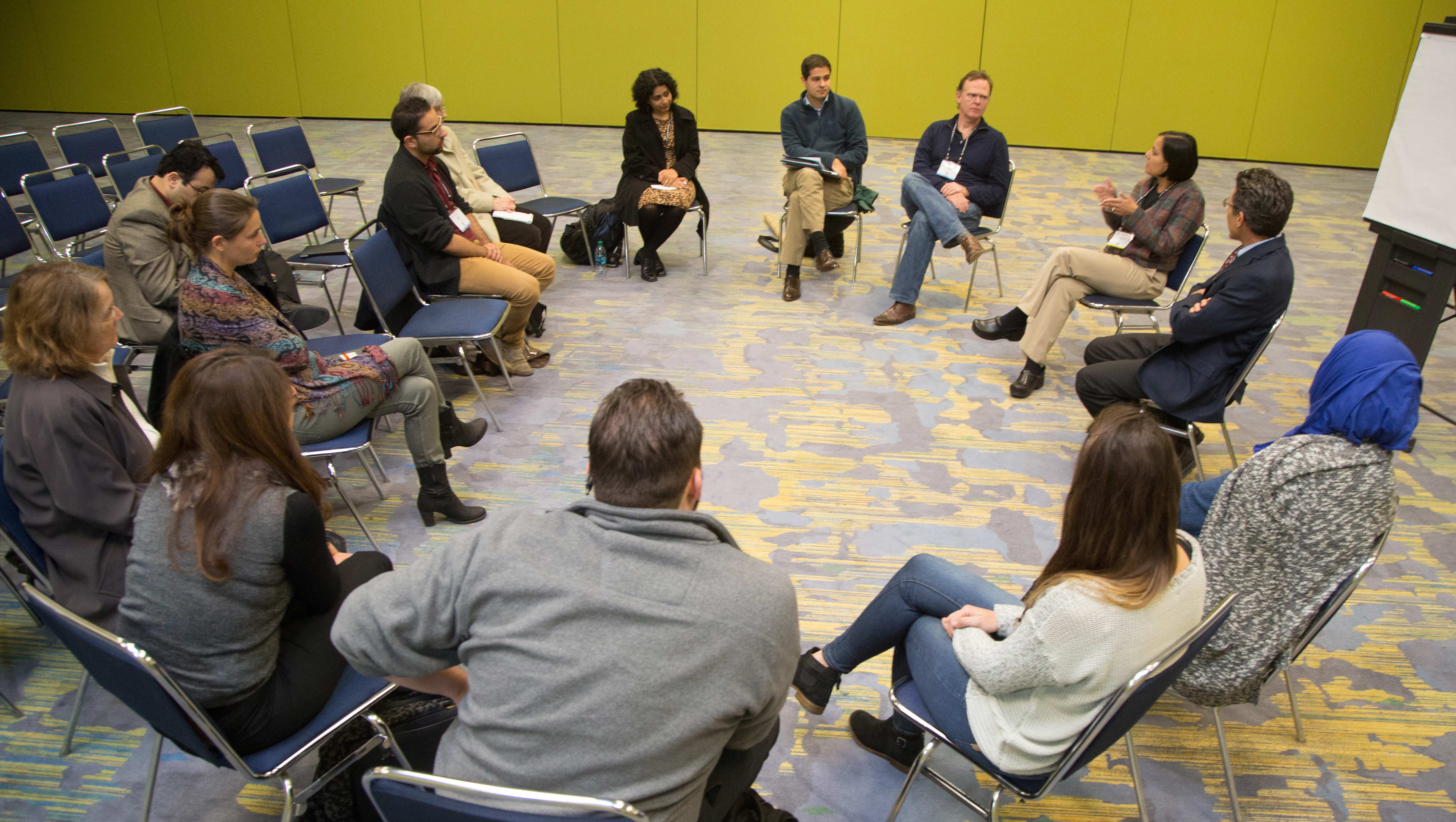A group of faculty and students sit in a circle and have a discussion. 
