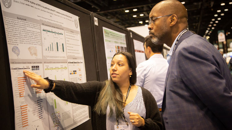 Image of a young woman explaining her poster presentation to a man at the SfN annual meeting.