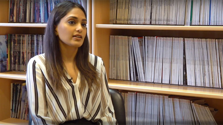 Devkee Vadukul sitting in front of a bookcase during an interview.