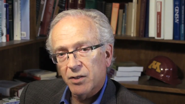 A man wearing glasses speaks to the camera.