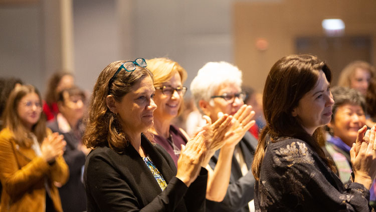 Women sit in rows applauding a speaker.