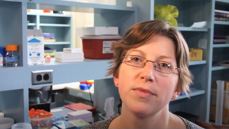 A woman wearing glasses speaks to the camera.