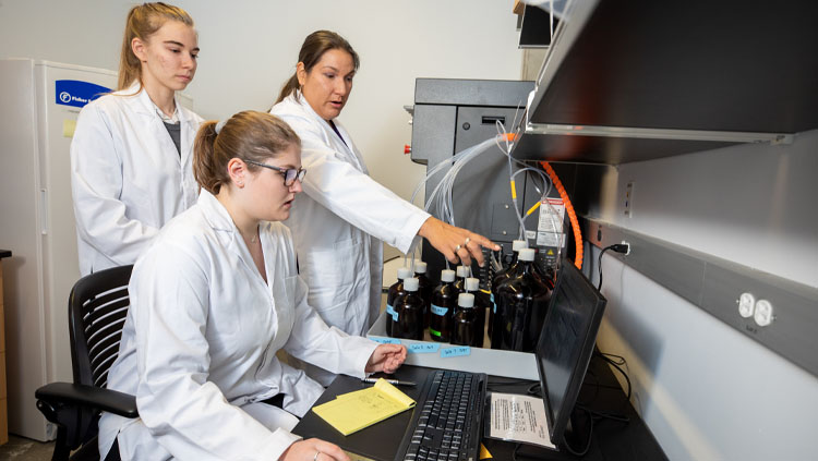 Naomi Lee instructs Jasmyn Genchev (BS, Chemistry, 2022) and Noelle Waltenburg (BS, Chemistry, 2020) how to use the Prelude X peptide synthesizer from Gyros Protein Technologies. Photo taken by NAU Marketing.