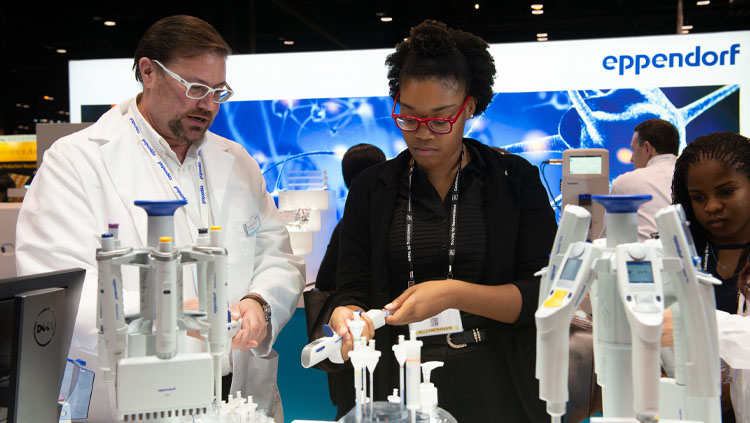 A man in a lab coat walks a woman through an instrument demonstration at Neuroscience 2019.