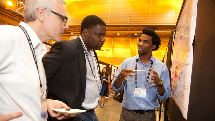 A scientist explains his research while two people intently listen.