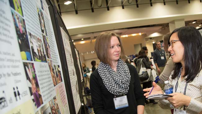 A female scientist explains her research to another female at a poster session. 