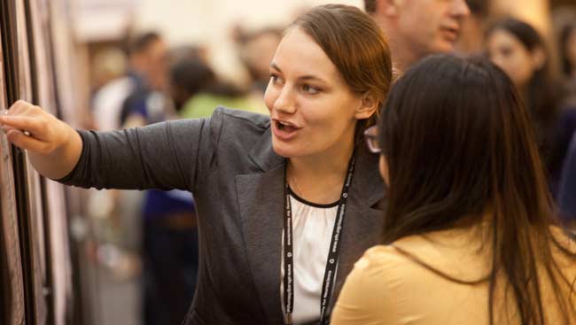 Female neuroscientist points to a scientific poster as she talks with another female neuroscientist at SfN's annual meeting.