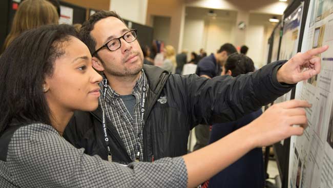 Two neuroscientists, female and male, point to a scientific poster. 