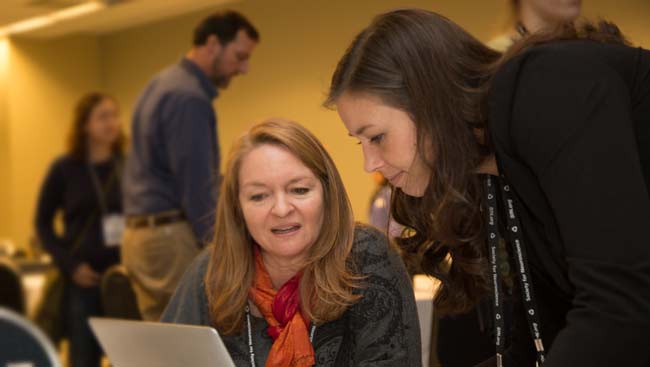 Two females share a computer screen. 