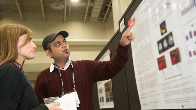 A male presents his scientific poster to a female colleague.