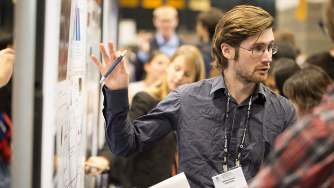 A male neuroscientist explains his research at a conference. 