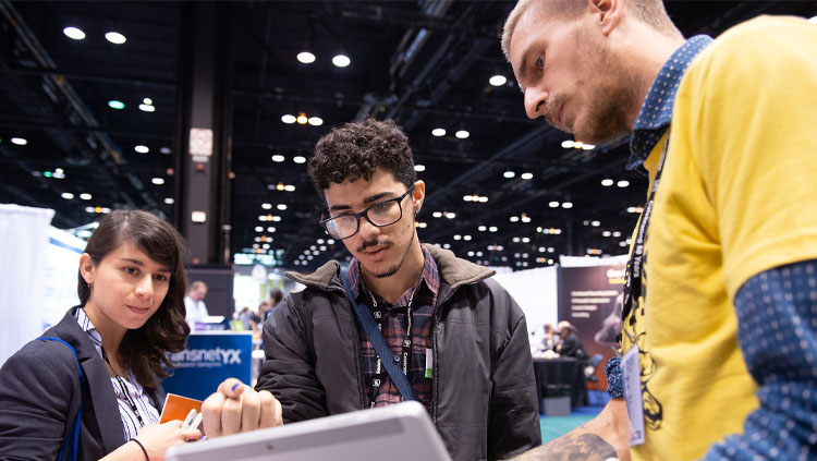 Three people look at a tablet screen and discuss it's contents.