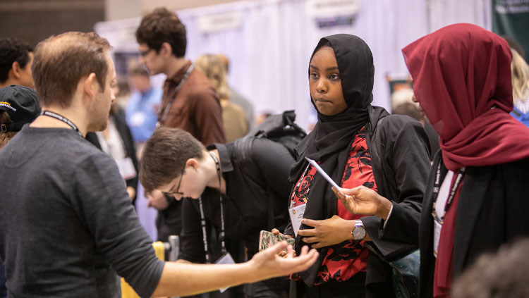 A man has a discussion with two women at the Neuroscience 2019 Graduate School Fair.