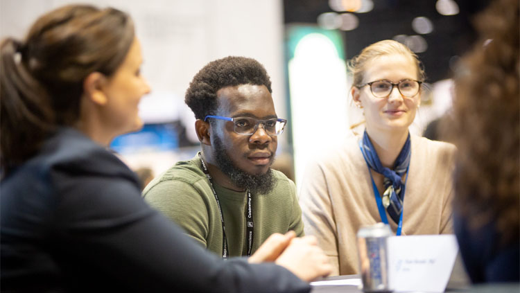 Three people sit at a round table having a discussion