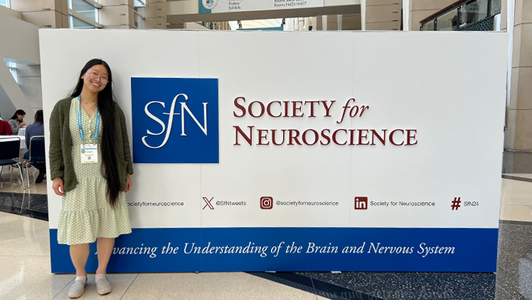 Tiffany Chan standing in front of the Society for Neuroscience logo at Neuroscience 2024 in Chicago.