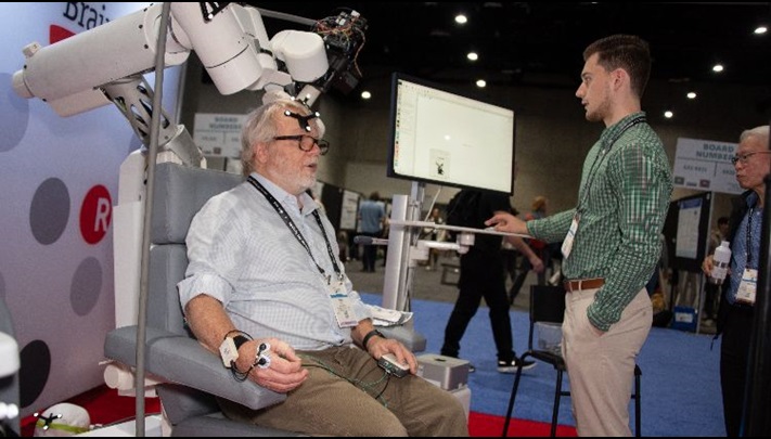 An attendee wearing sensors participates in a neuroscience exhibit demonstration beside a robotic arm.