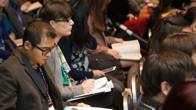 A male attendee takes notes during a lecture. 