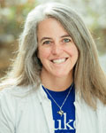 Headshot of Anne West wearing a blue shirt with a while jacket