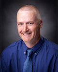 Headshot of Brandon Prestwood wearing a blue button down shirt with a blue tie.