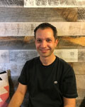 Image of Lenny Teytelman standing in front of a wood paneled wall wearing a black shirt. 