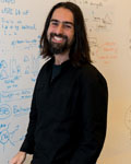 Manuel Mameli standing in front of a whiteboard wearing a black button up shirt.