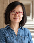 Image of Zhuzhu Zhang standing in front of a stone wall wearing a denim shirt.